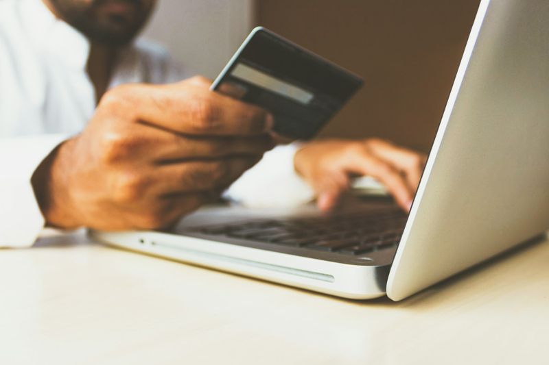 Pessoa segurando cartão de crédito diante de um notebook