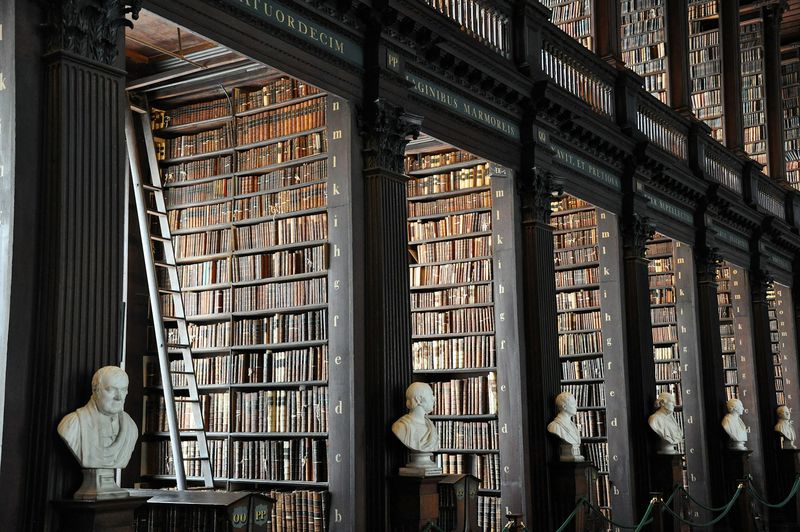 Biblioteca histórica com longas estantes de livros e bustos de mármore